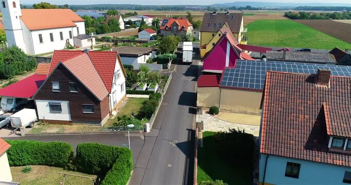 A white truck drives through a small town. Truck rides on a narrow European street aerial view. Truck delivers goods through narrow European streets