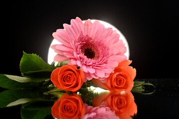 Beautiful orange roses surrounded by stunning floral arrangement in a studio setup on a reflective surface with light from behind. Inspirational as roses are the flower of love