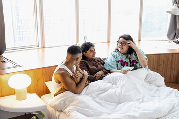 Obraz premium Three friends chatting and laughing together at home in bed