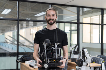 Fototapeta na wymiar Portait of male engineer holding compact desktop robotic arm for for manufacturing lines in workshop. Smart automation tasks concept