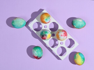 Colored Easter eggs in tray on purple background with shadow. Creative layout