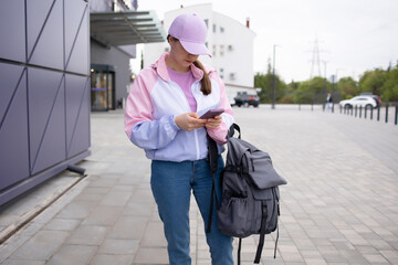 Woman of 20-25 years old in a sports jacket, jeans and a purple baseball cap with a backpack looks...