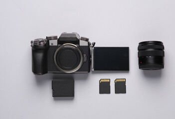 Modern digital camera with flip screen, two sd memory cards, battery and lens on gray background....