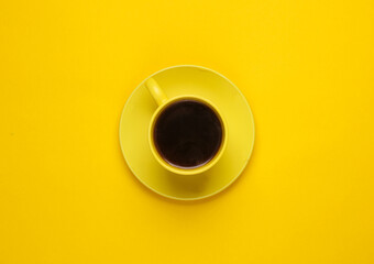 Yellow ceramic cup with coffee on a saucer, yellow background. Top view