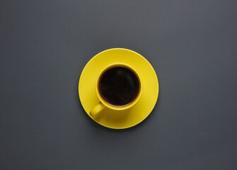 Yellow ceramic cup with coffee on a saucer, dark gray background. Top view