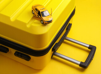 Yellow travel suitcase and toy taxi car on a yellow background