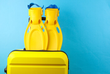 Yellow plastic travel suitcase with diving fins on blue background. Summer rest, beach vacation,