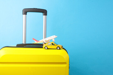 Yellow plastic travel suitcase and toy taxi car, air plane on blue background. Tourism, vacation...