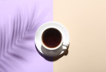 Ceramic cup with coffee and shadow from palm leaf on pastelbackground. Creative layout. Top view