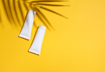 Two white cream tubes on yellow background with palm leaf shadow. Creative beauty layout. Top view. Copy space