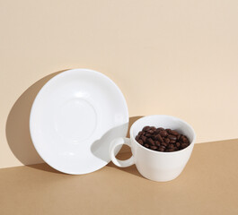Ceramic cup with coffee beans and saucer on a brown backgroun with shadow. Creative layout