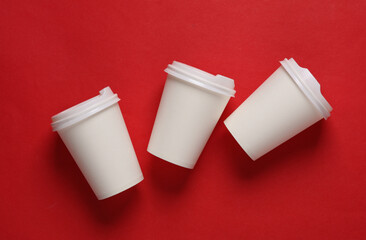 Mockup of white disposable cups with lids for hot drinks on red background