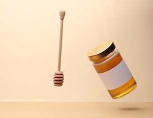 Jar of honey with a white label and spood levitation on beige background