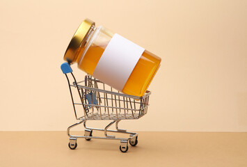 Mini supermarket trolley with jar of honey on a two-tone beige background