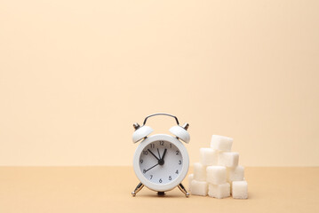 Sugar cubes with alarm clock on beige background