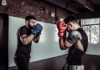 Two sparring partners of a kickboxer in boxing gloves practice kicks in a sports hall