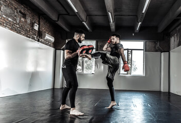 Male fighter trains punches with partner with training boxing paws