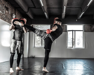 Male fighter training kicks with partner with training boxing paws
