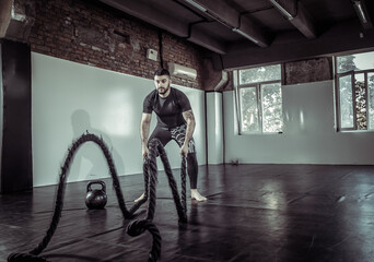 Male athlete trains with battle ropes in a sports hall