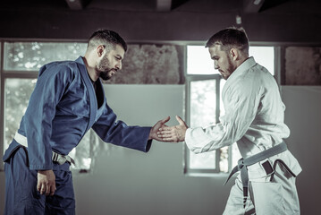 Two fighters in kimono greet each other before a sparring fight in a sports hall