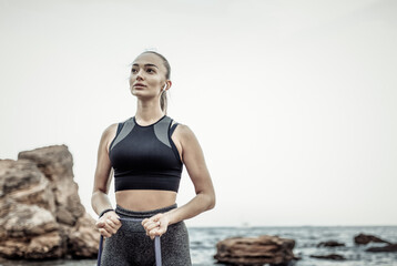 Young fit woman in sportwear training with a fitness elastic band (expander) on a wild beach