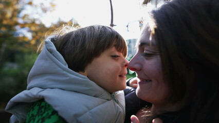 Happy mother and child doing eskimo kiss with nose standing outdoors with sunlight flare....