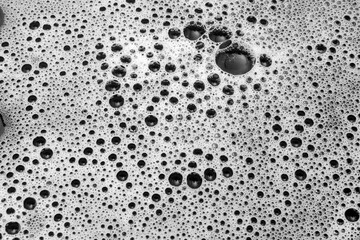 Detalhe de espuma branca de sabão sobre uma superfície preta.