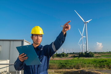 Asian Man engineers working and holding the report at wind turbine farm Power Generator Station on mountain,Thailand people,Technician man at site of work