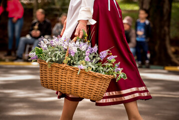 Woman in old dress parading, woman carrying basket of flowers