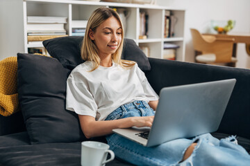 A cute young woman sitting on the sofa and working on her laptop.