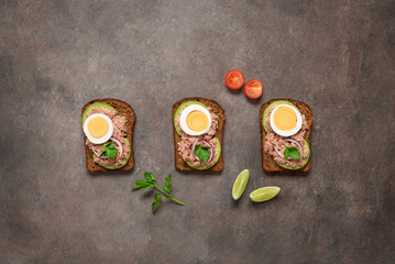 Obraz na płótnie Canvas Open sandwiches with tuna, avocado and boiled egg in a row on a brown background. Top view, flat lay. Toast with tuna and rye bread.