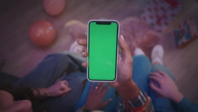 A woman's hands holding green screen phone in her lap close up. A girl at a party shows something, scrolls to her friends on the phone, the girls point with their index fingers, and show a thumbs up.