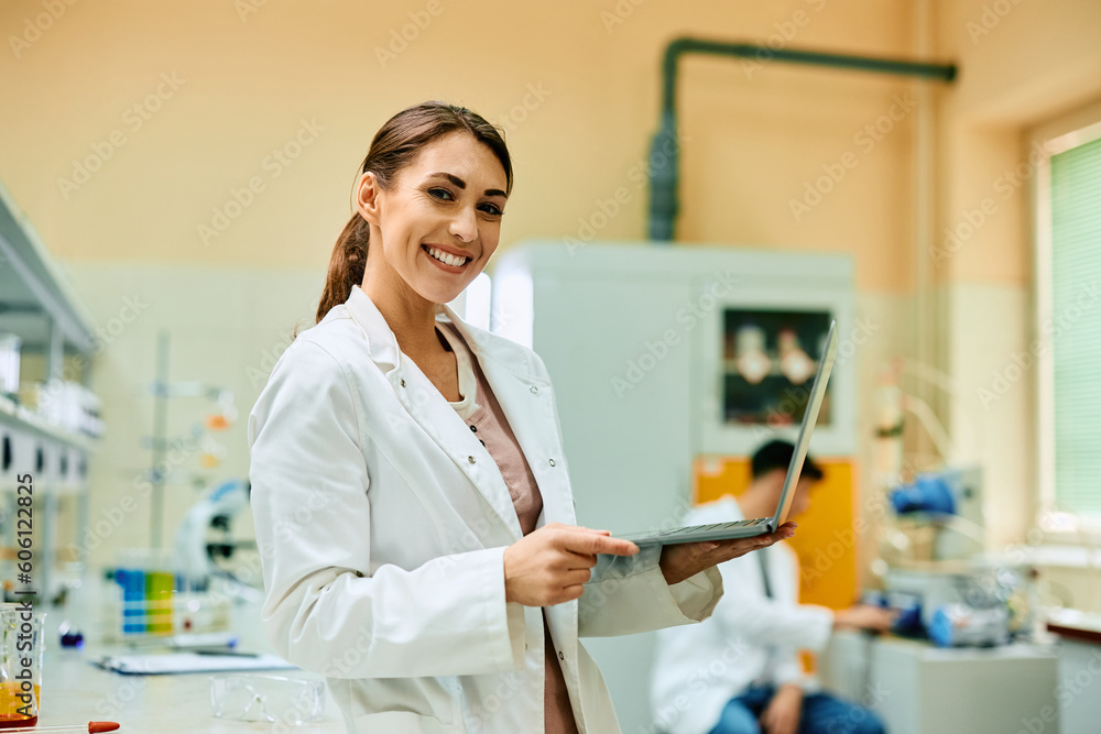 Wall mural happy female scientist using laptop while working in lab and looking at camera.