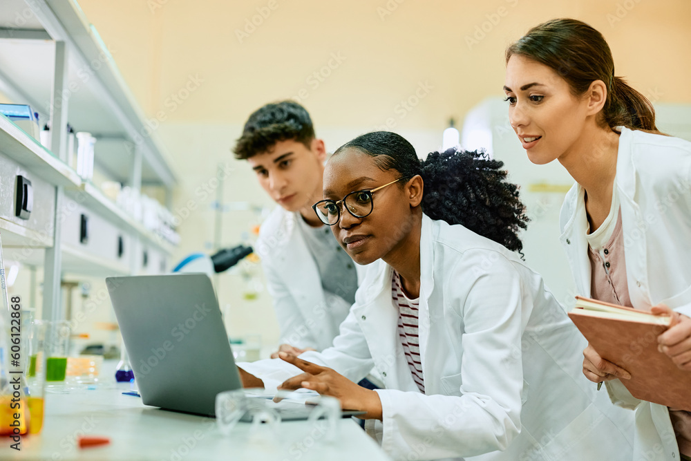 Wall mural team of young scientists using laptop while working on new research in lab.
