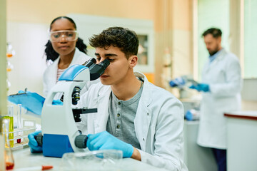 Young biochemist looking through microscope during research in lab.
