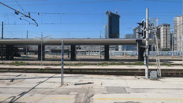 Looking out of a train window as the tracks go by with a view of Naples, Italy under a blue sky.