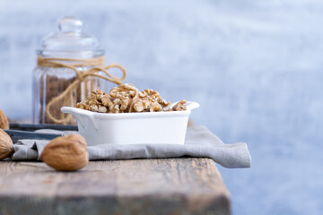 A close-up of walnuts on a blurry background. The walnuts are arranged in a white dish on a vintage rustic wooden table, and the background is soft and blurry.