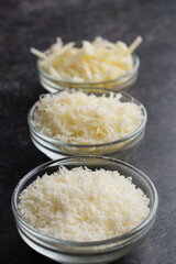 Freshly Grated and Shredded Parmesan Cheese in Glass Prep Bowls: Three different textures of grated parmesan cheese with the finest texture in front