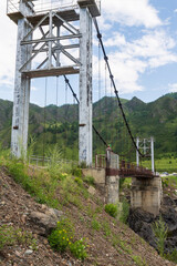Oroktoysky Bridge - road suspension bridge over rocky banks of Katun River in green valley of Altai Mountains. Popular landmark in Chemal district of Altai Republic, Siberia, Russia