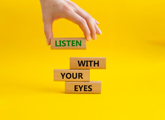 Listen with your eyes symbol. Concept word Listen with your eyes on wooden blocks. Beautiful yellow background. Businessman hand. Business and Listen with your eyes concept. Copy space