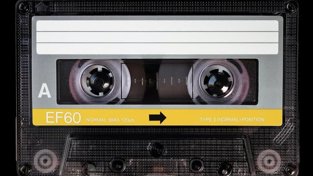 Audio cassette tape in use for sound recording in the tape recorder. A vintage, brand new blank yellow labelled music cassette playing back in a deck player. Static video camera shot. Close up, 4K
