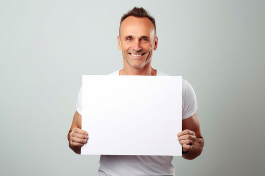 Portrait of a smiling man holding a blank sheet of paper on grey background