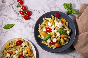 Fresh pesto pasta salad with different colours of cherry tomatoes and mozzarella with a light...
