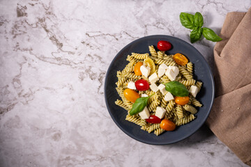 Fresh pesto pasta salad with different colours of cherry tomatoes and mozzarella with a light background.