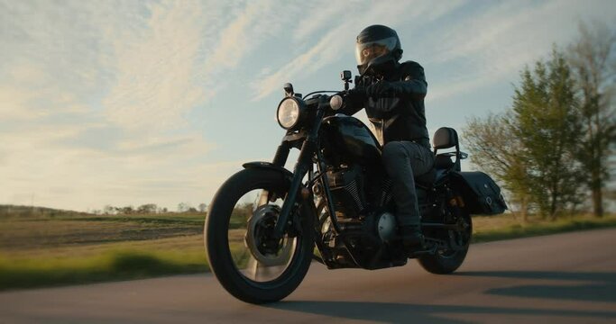 Low-angle tracking shot of a biker riding a motorcycle through a country road. 
