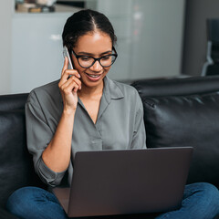 Young woman talking on mobile phone while working on laptop at home