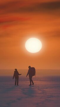 The two tourists walking through the snow field on sunset background. slow motion