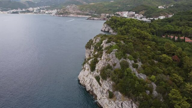 Aerial view over cliff, King's Beach, Milocer Beach with green park and Sveti Stefan, Saint Stephen, island in Montenegro in Adriatic sea. Located at the foot of mountain chain. Popular tourist spot.