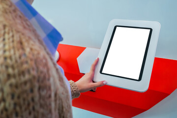 Woman looking at blank vertical interactive touchscreen white display of electronic tablet kiosk at...