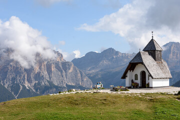 Old couple sitting on a bench near a little church looking to dolomites mountains in Italy